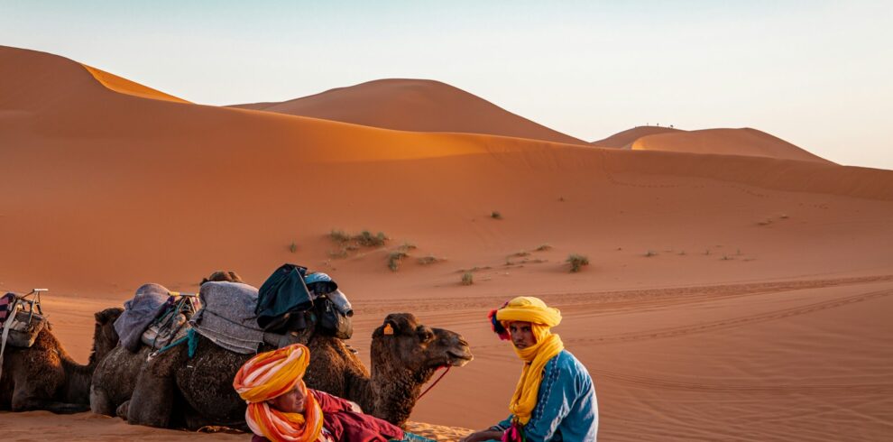 man in yellow robe sitting on brown sand during daytime